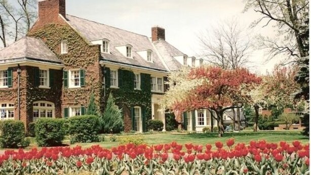 A large brick house with a symmetrical facade, green shutters, and a well-maintained garden with red tulips. - Montague Inn (Saginaw)