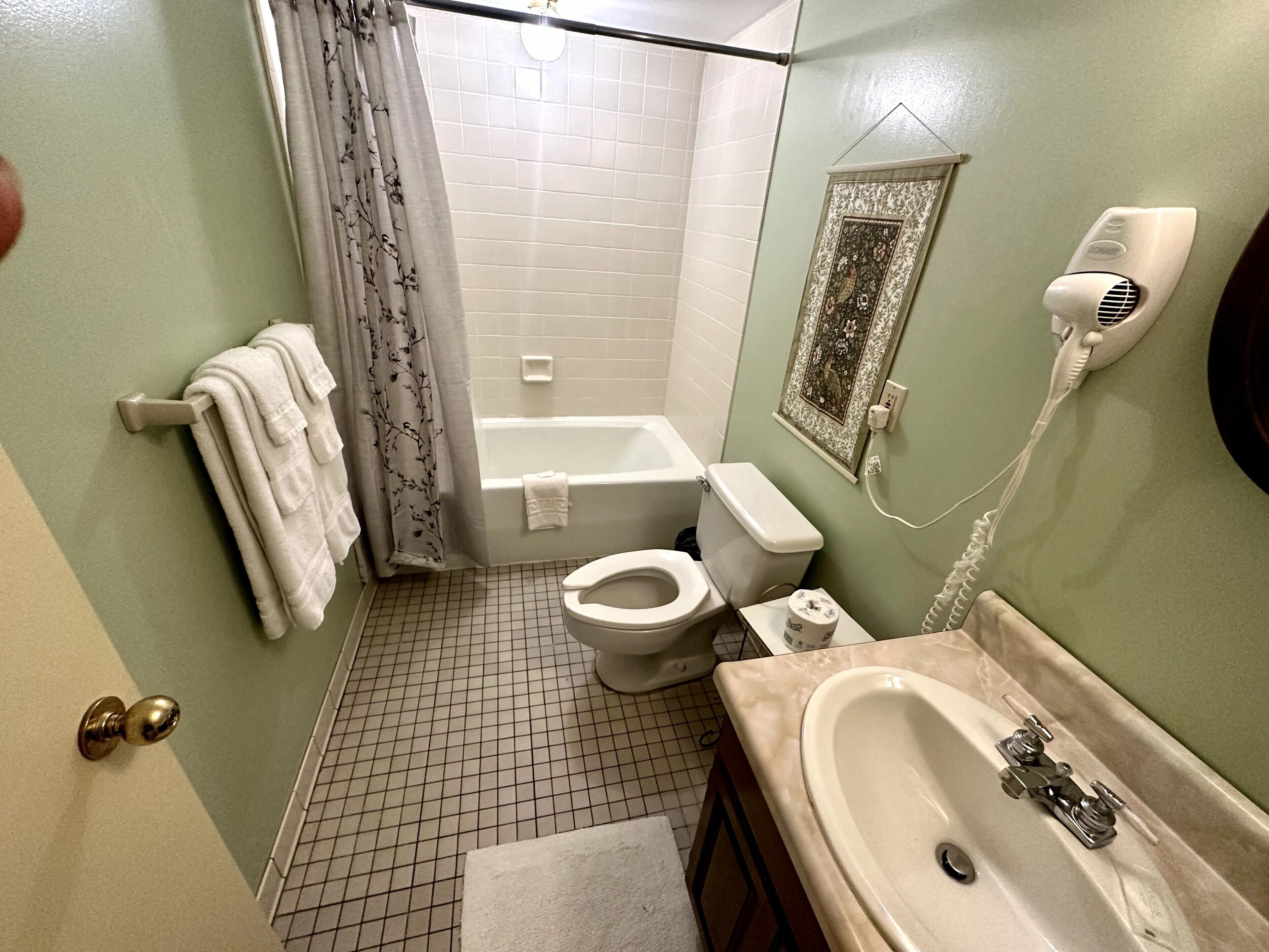 Un baño con bañera, inodoro, lavabo y un secador de pelo en la pared.