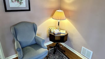Habitación de esquina con un sillón azul, una mesita de noche con lámpara, un cuadro enmarco y una alfombra estampada.