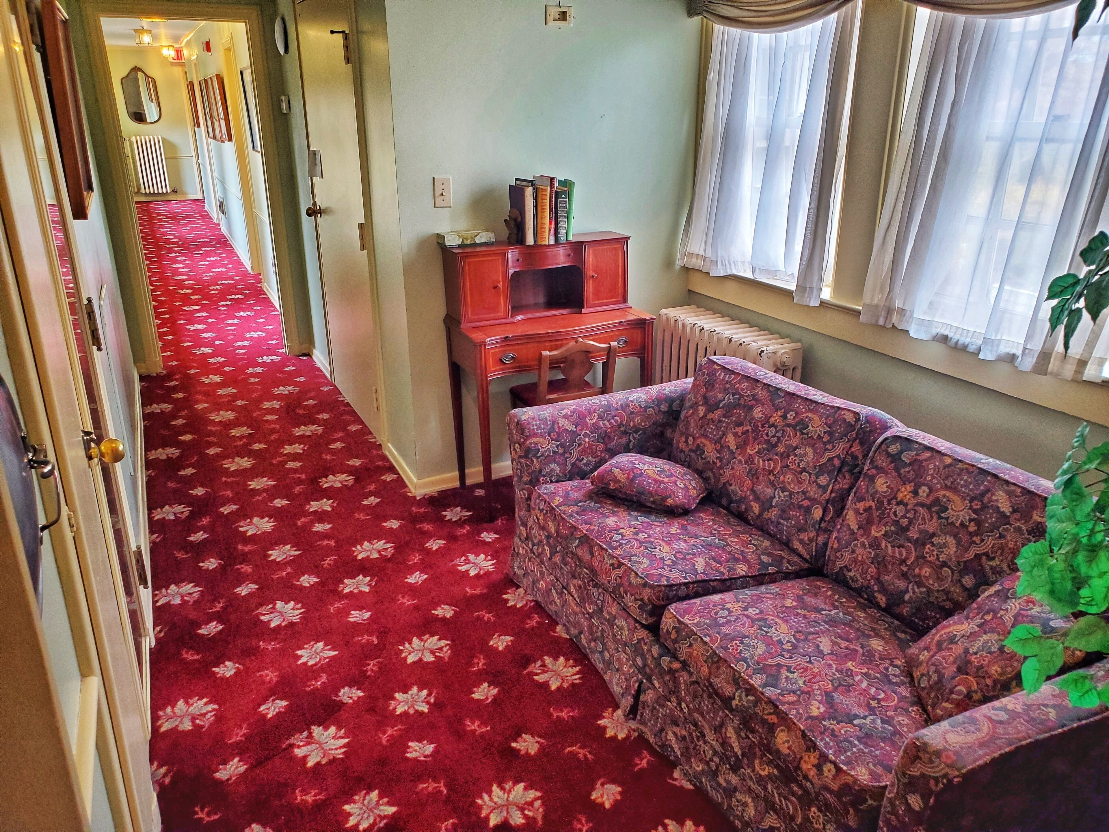 A hallway with a red carpet, a patterned sofa, a wooden cabinet, and a radiator.