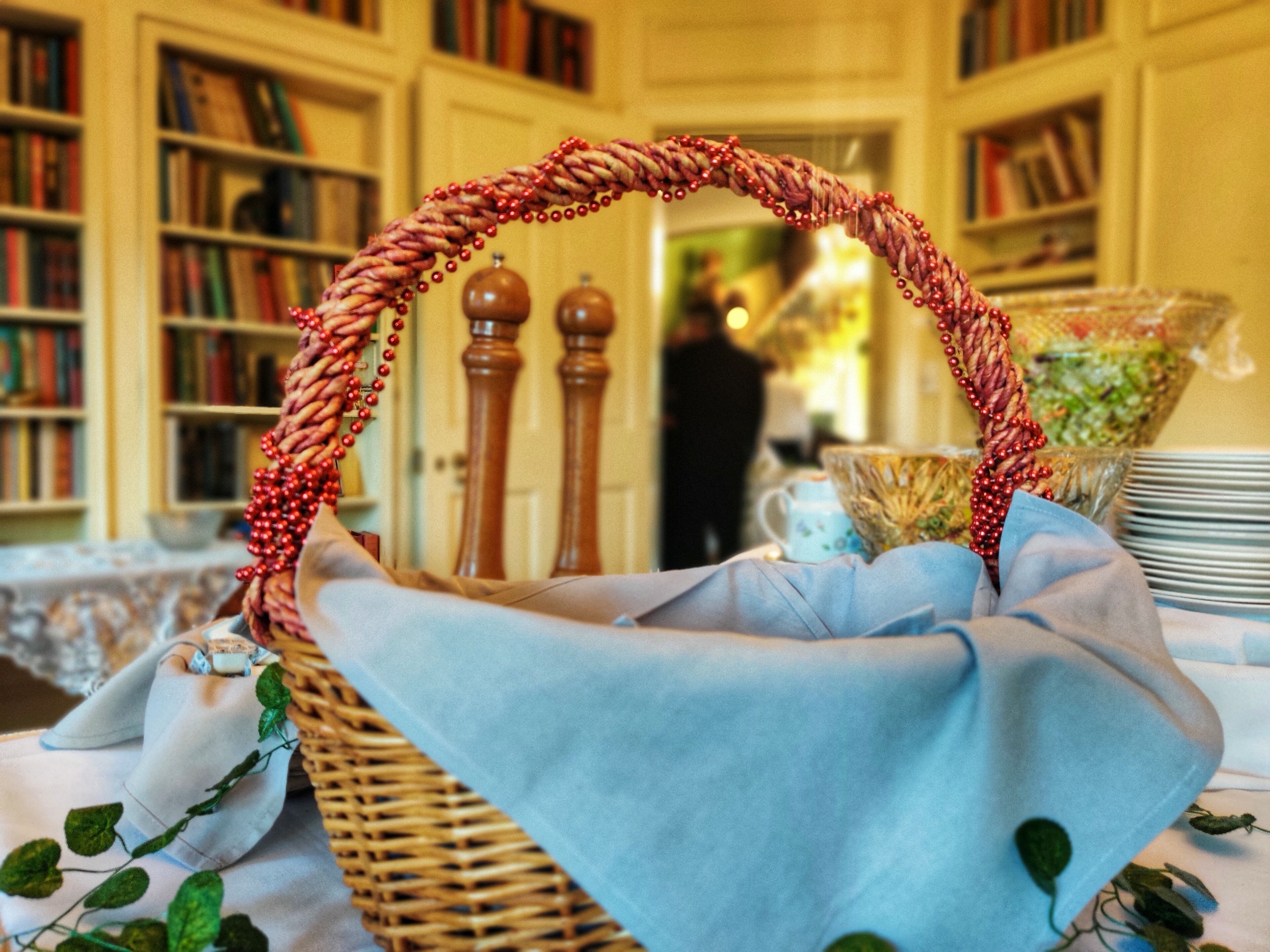 A wicker basket with a handle, placed on a table with a blue cloth.