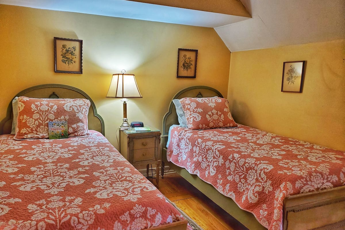 Quarto com duas camas, cada uma com roupa de cama estampada com flores, mesa de cabeceira com abajur e obras de arte com motivos florais emolduradas nas paredes.