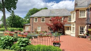 A brick building with a central courtyard, surrounded by lush greenery and potted plants. - Montague Inn (Saginaw)