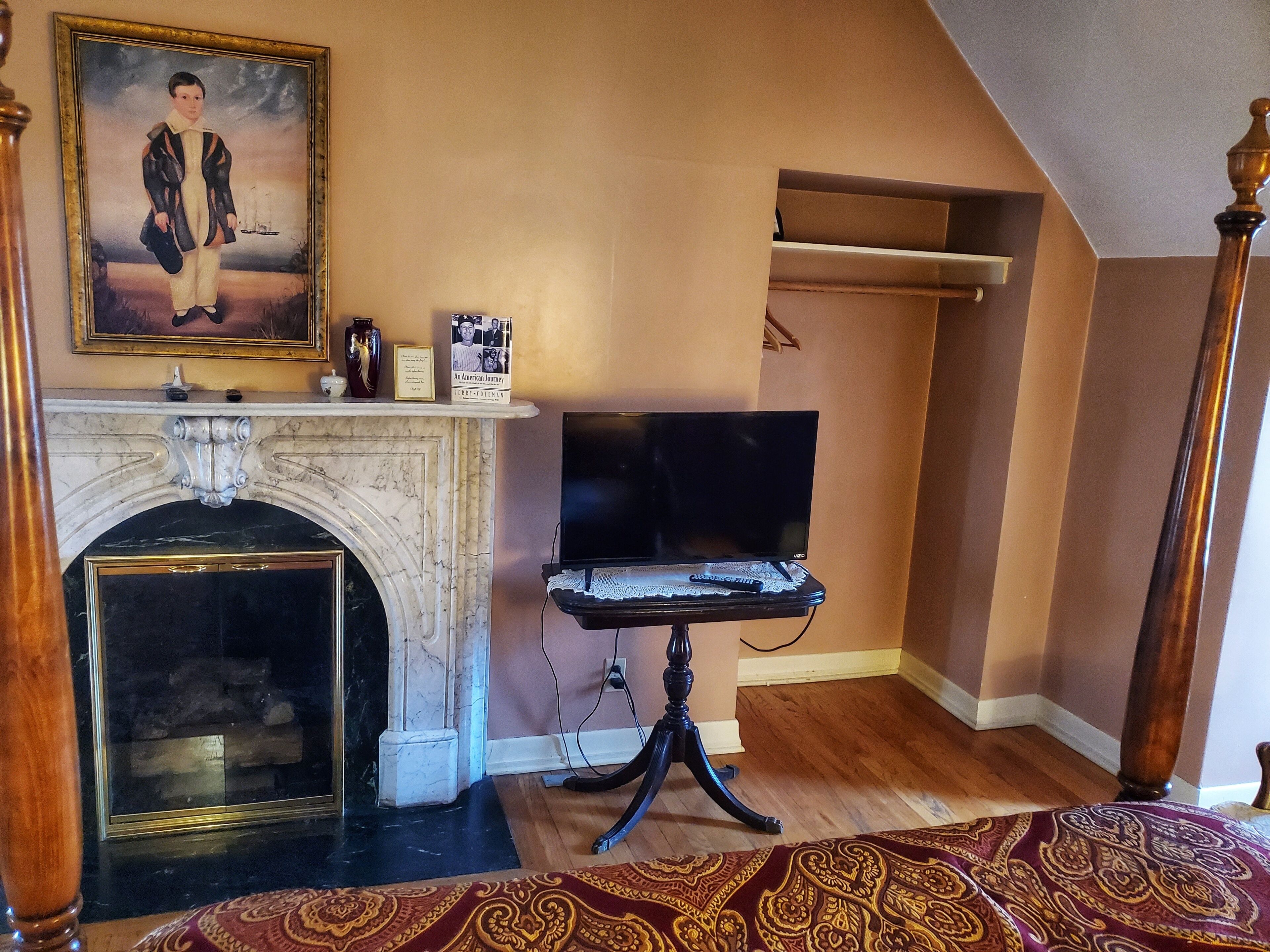 Une pièce avec une cheminée, un téléviseur posé sur un meuble, un tapis à motifs et un tableau accroché au mur.