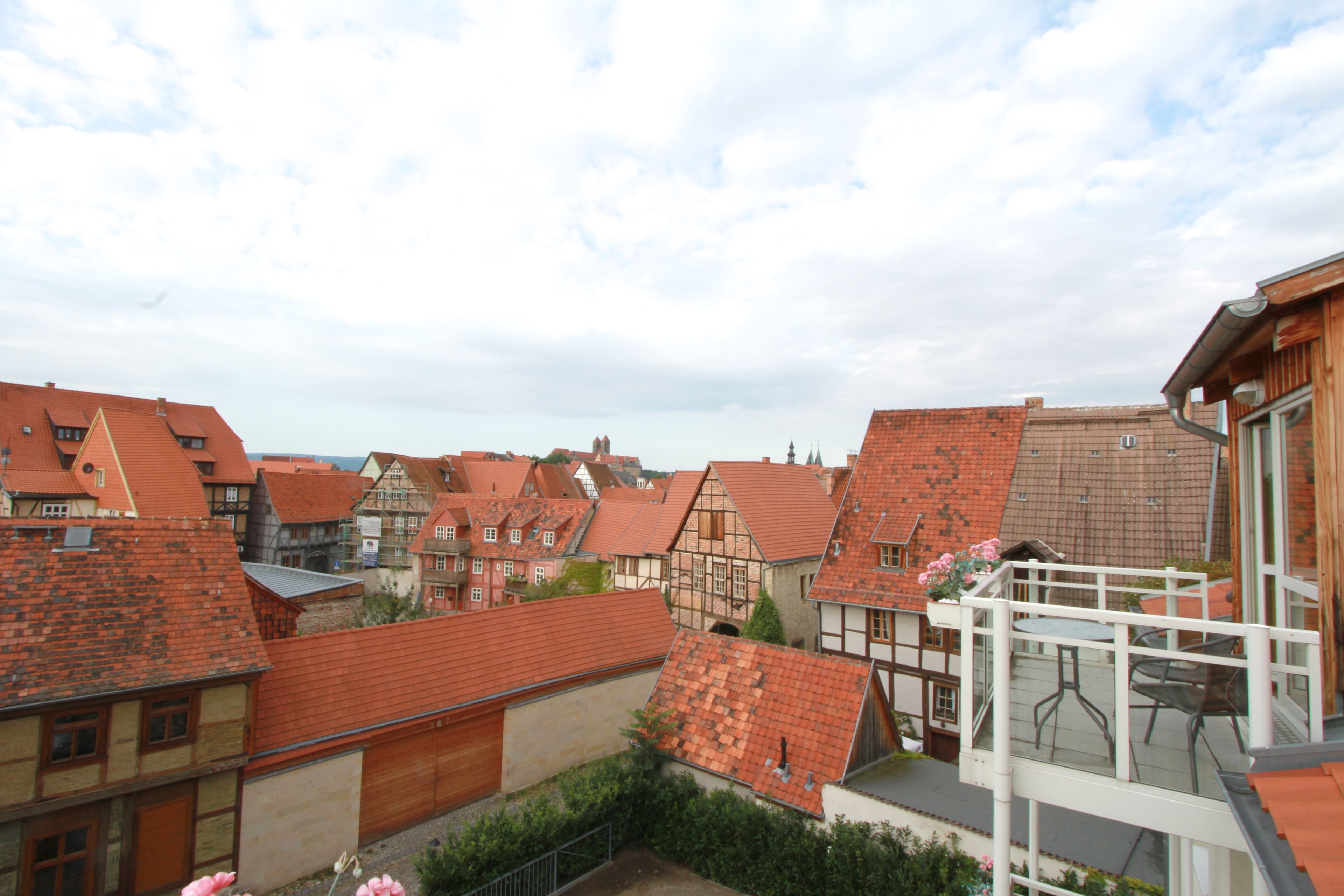 A residential area with traditional half-timbered houses, a balcony with a table and chairs, and a clear sky.