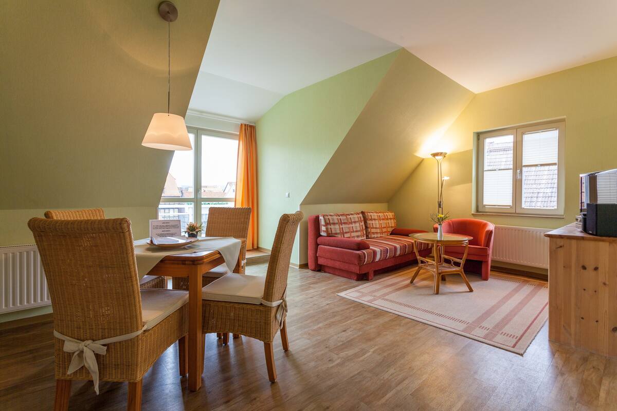 Ein Essbereich mit Korbstühlen, einem Tisch, einem roten Sofa und einer Lampe.