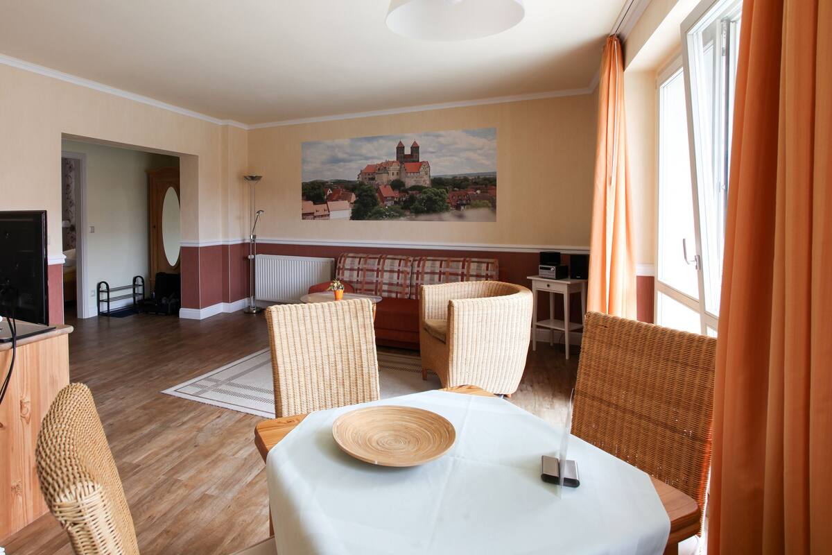 Ein Essbereich mit Korbstühlen, einem Tisch mit weißem Tuch und einem Gemälde eines Schlosses an der Wand.