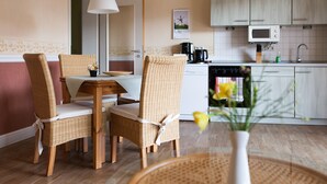 A cozy kitchen with wicker chairs, a dining table, a white microwave, and a sink.