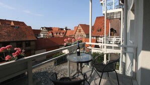 A balcony with a table and chairs, a bottle of wine, and pink flowers.