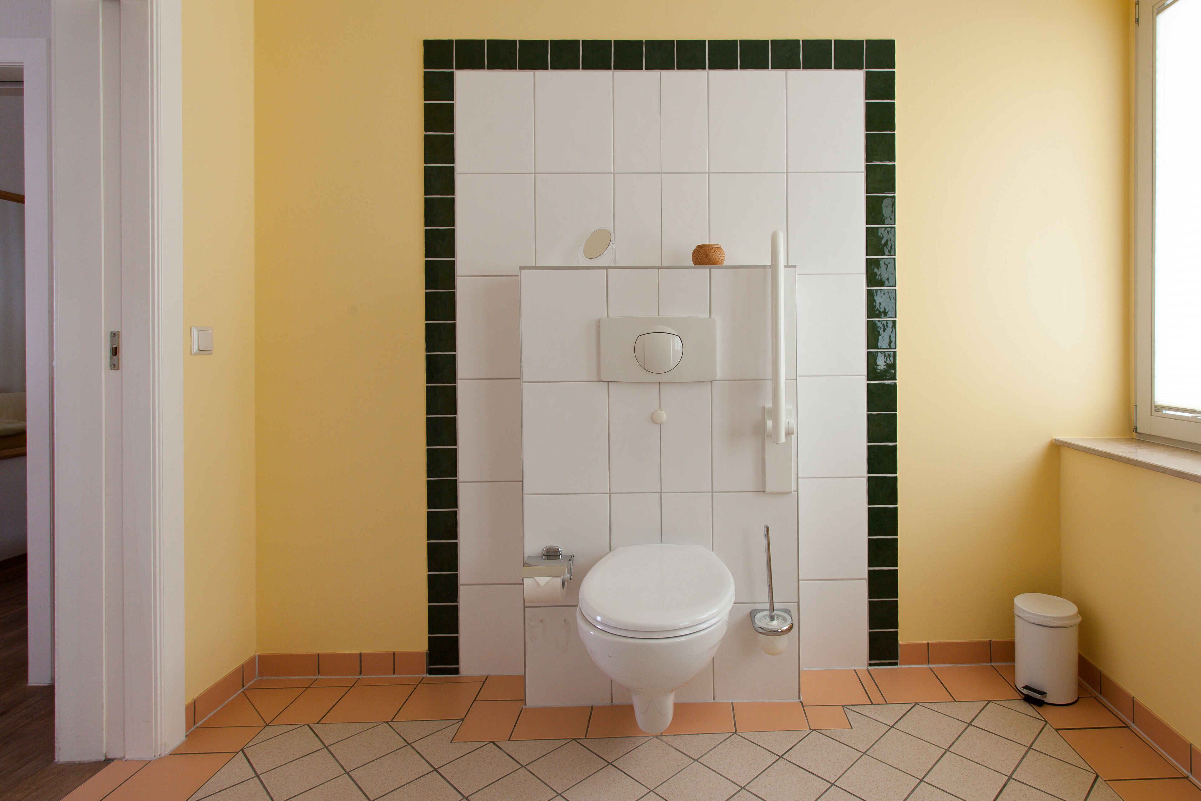 Een badkamer met een toilet, een handdroger, een prullenbak en een klein plankje met een fles.