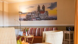 A cozy living room with a large painting of a castle, a sofa with striped cushions, a small side table with a vase of flowers, and a lamp.
