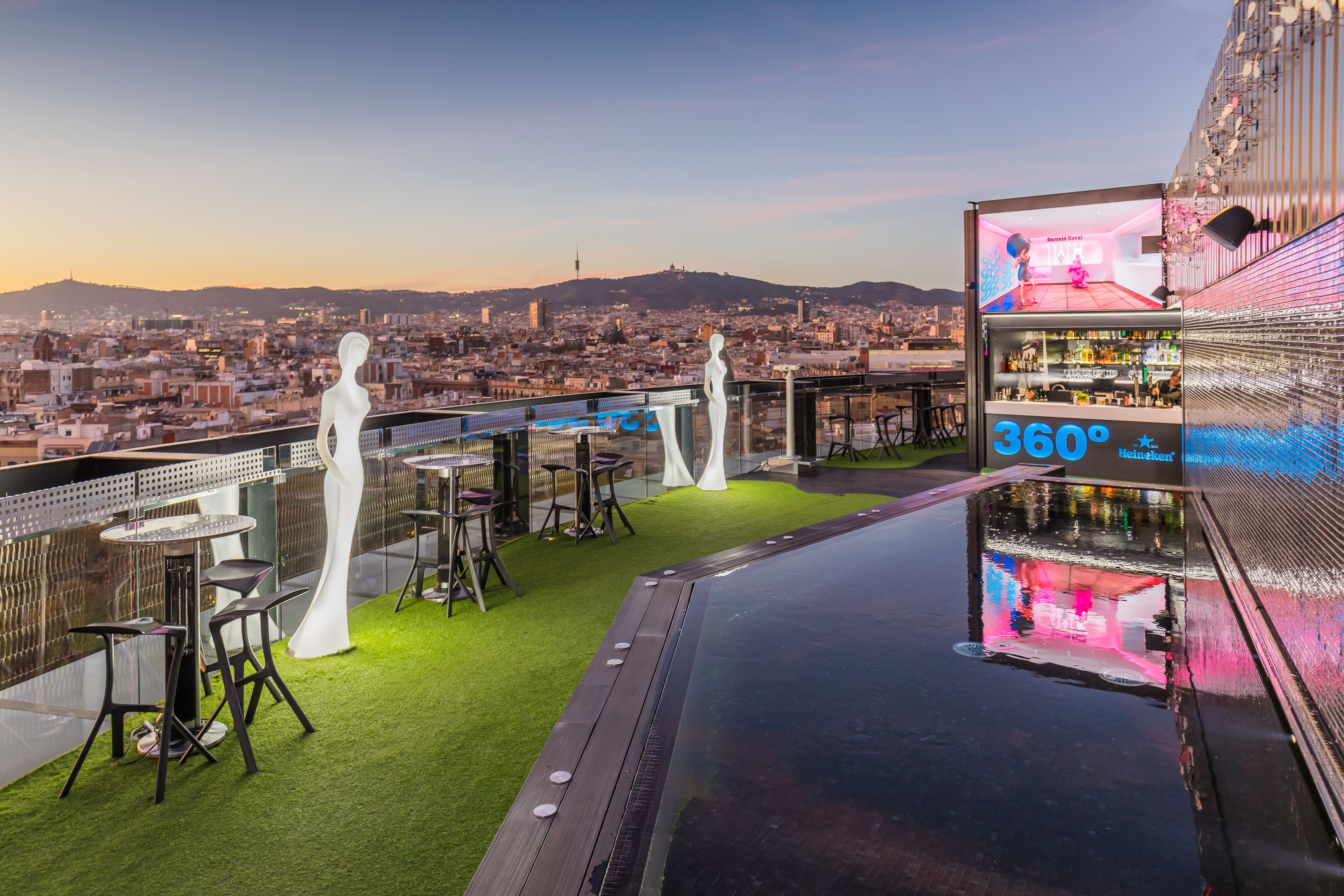 A rooftop bar with a panoramic city view, a glass railing, and a bar area with a 360° sign.