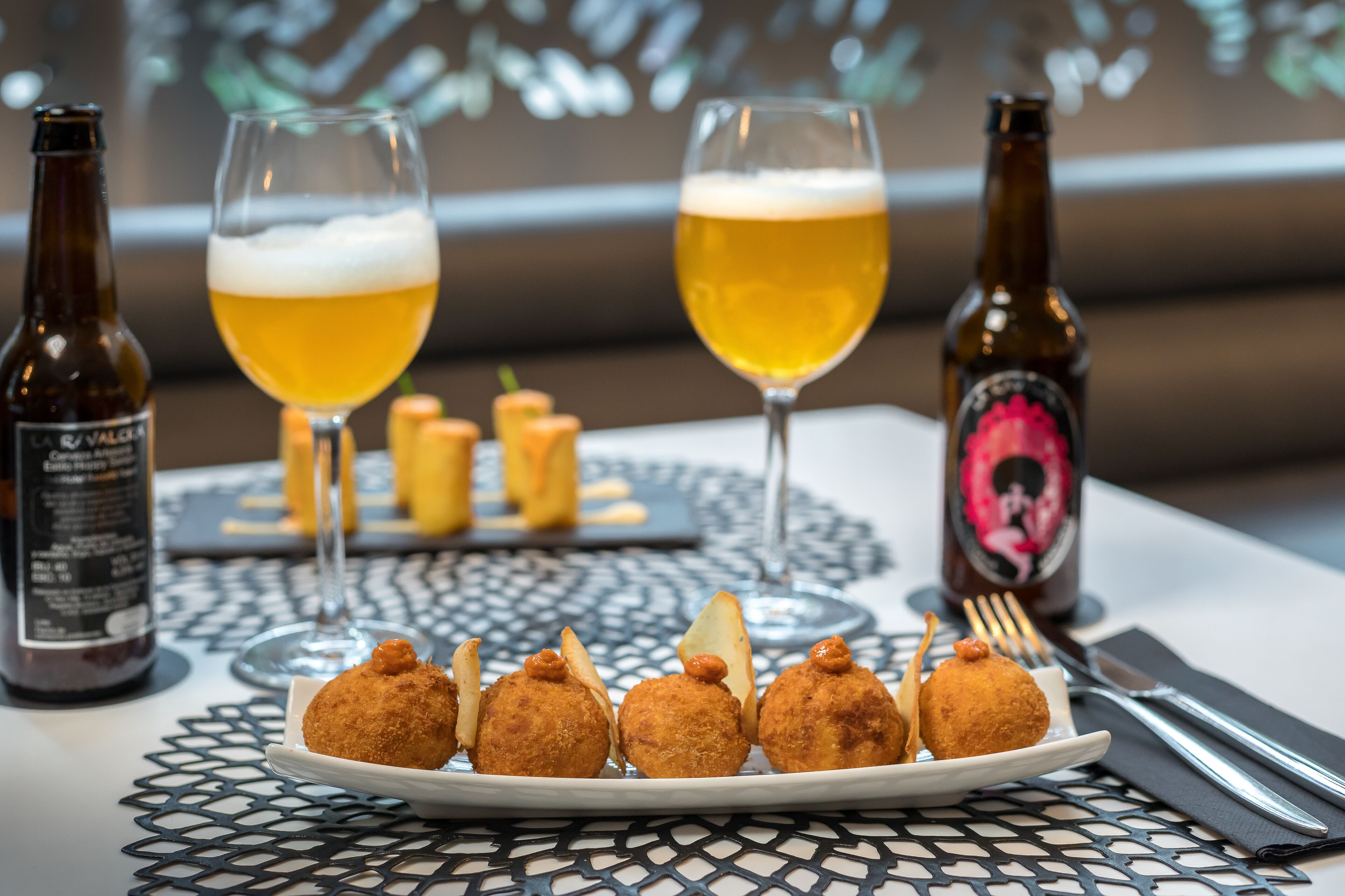 Uma mesa com duas cervejas em copos, uma garrafa de cerveja e um prato de comida frita.