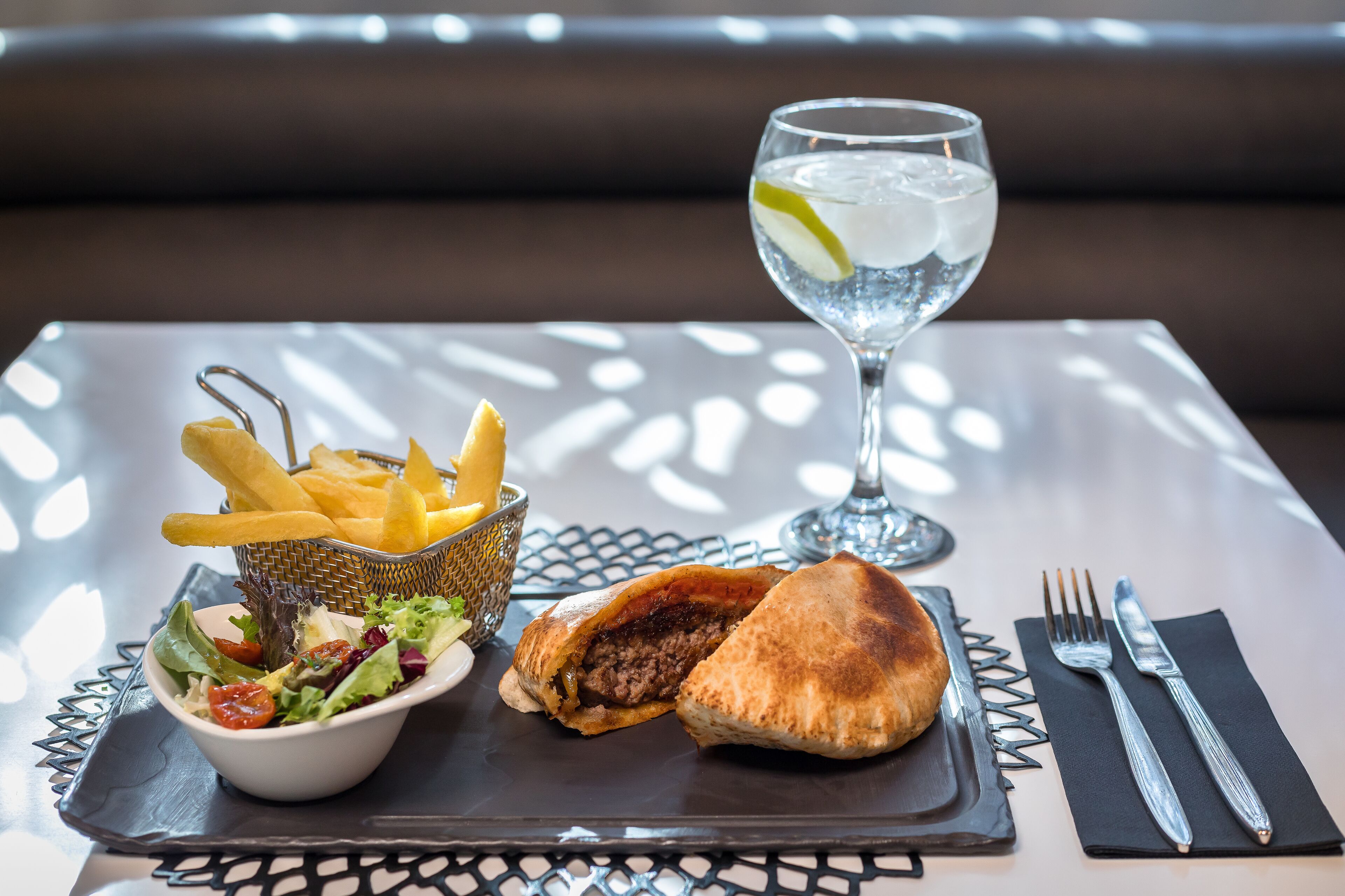 A meal consisting of a sandwich, fries, and a salad on a table with a glass of water and cutlery.