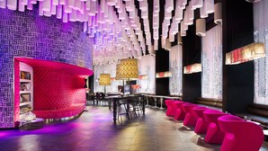 A modern bar area with a curved seating arrangement, a patterned wall, and hanging pendant lights.