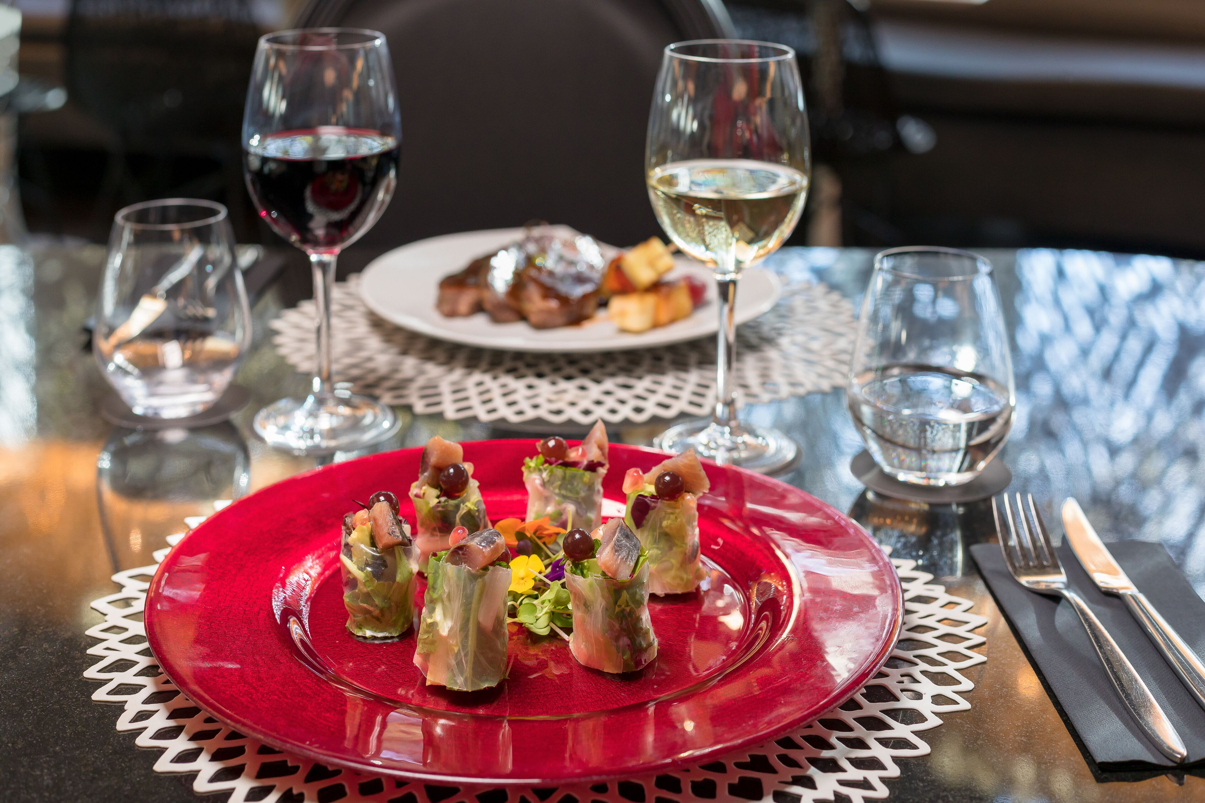Una mesa con un plato rojo de aperitivos, dos copas de vino y cubiertos.