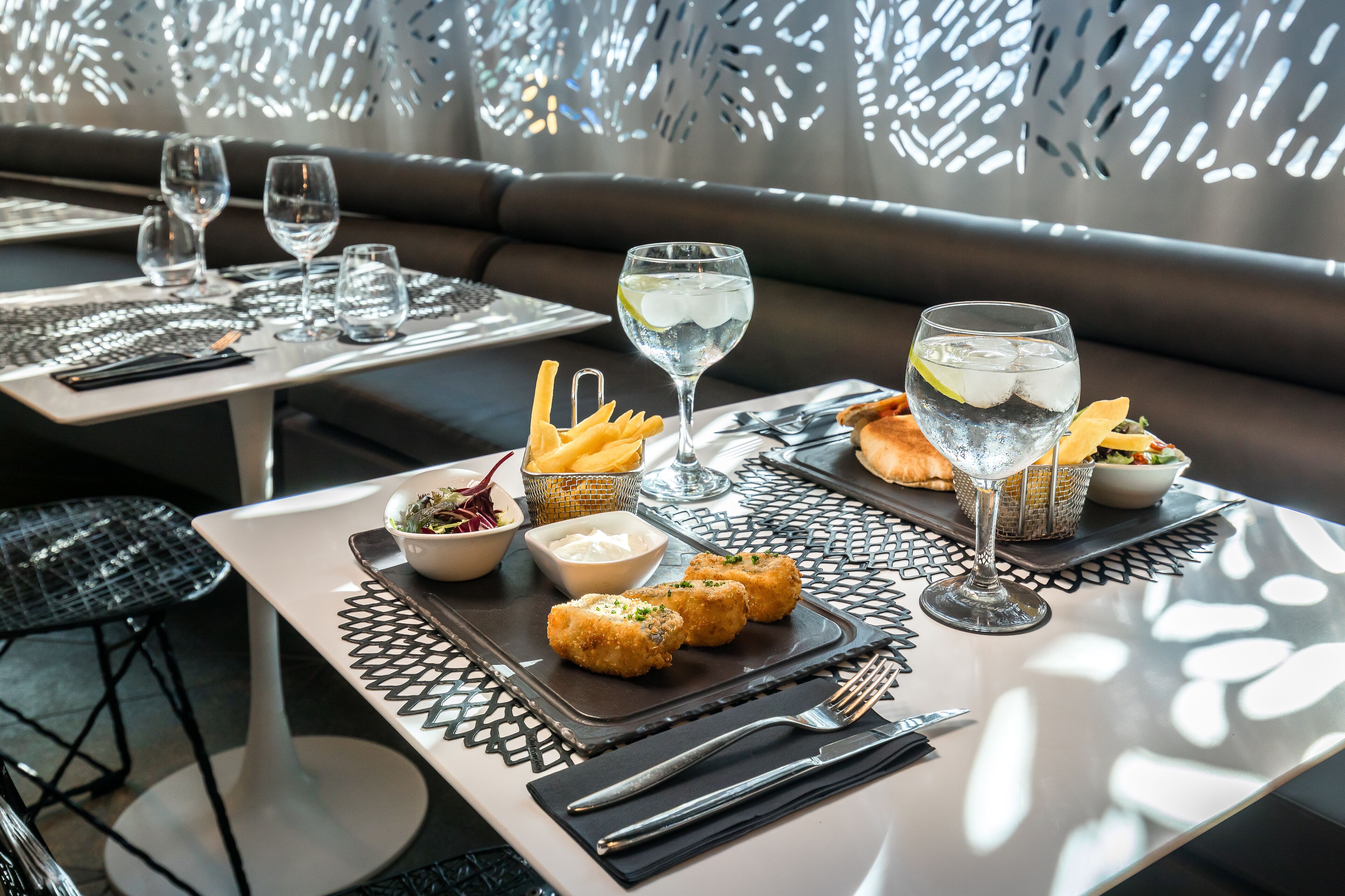 A dining table set with a glass of water, a glass of white wine, a bowl of salad, a small bowl of sauce, and a plate of fried food.