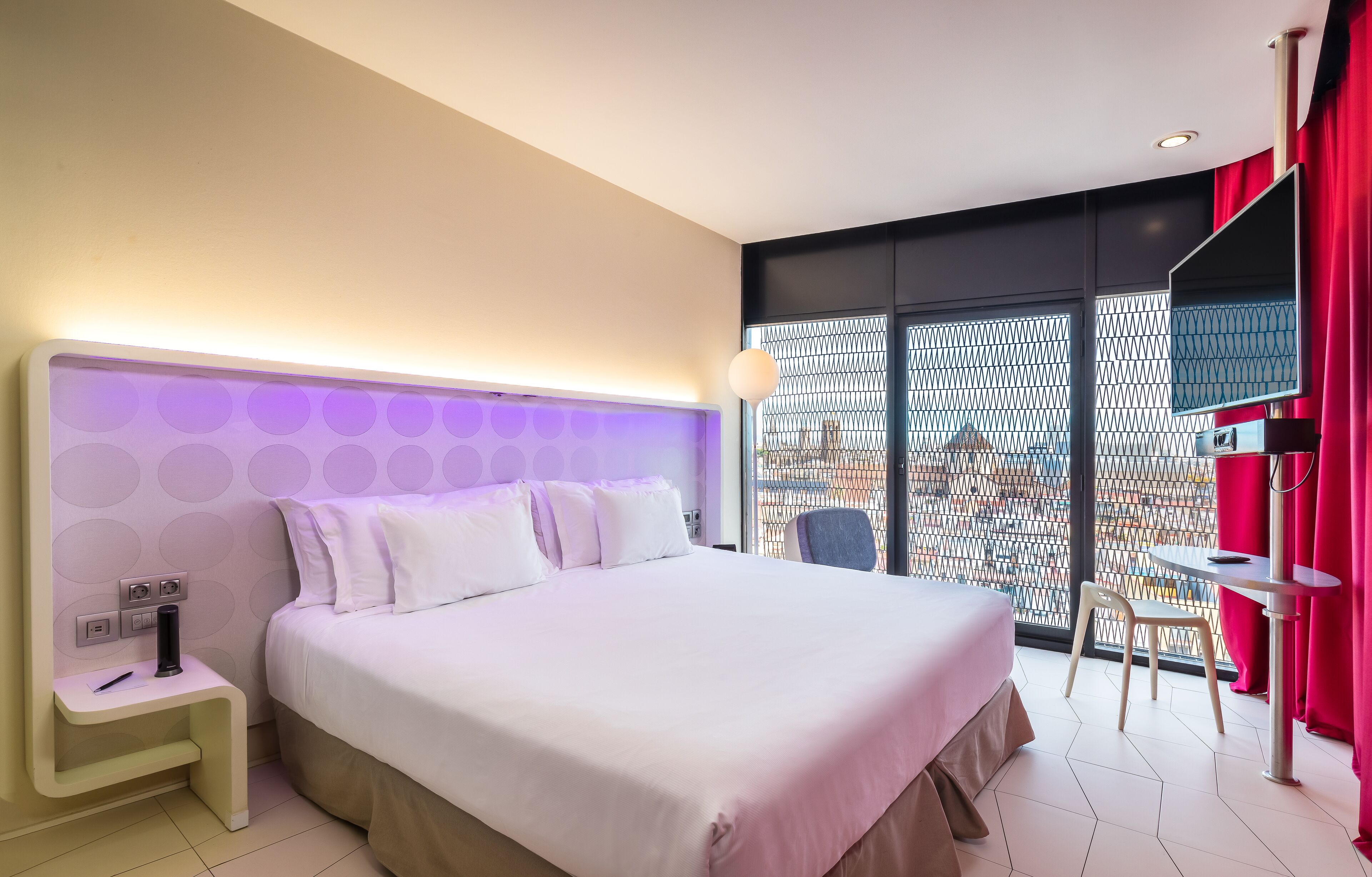 A modern hotel room with a large bed, a small table, and a chair.
