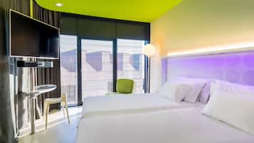 A modern hotel room with a large bed, a flat-screen TV, a small table, and a green chair.