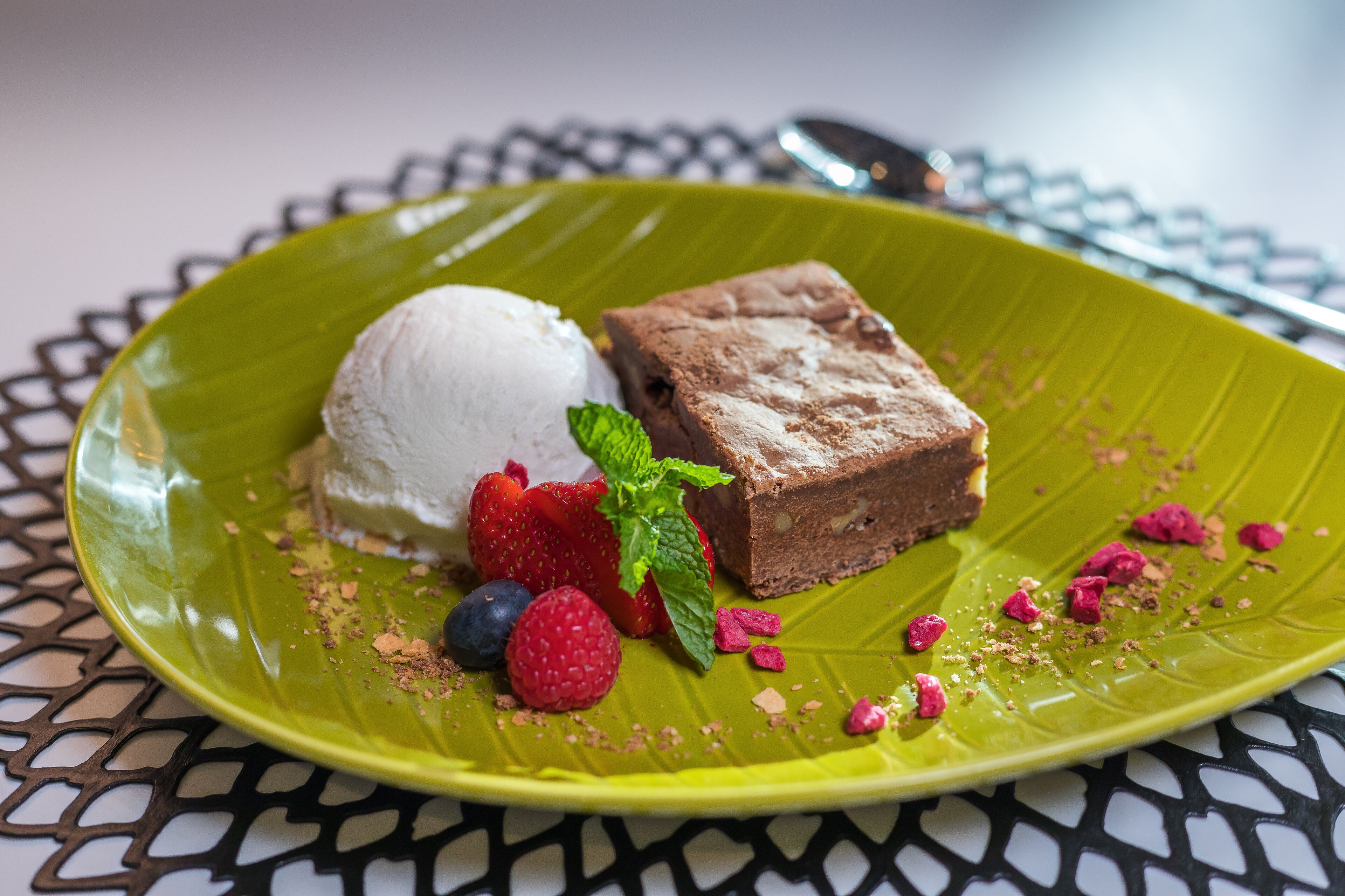 Ein Dessertteller mit einer Kugel Vanilleeis, einem Stück Schokoladenkuchen, Erdbeeren, Himbeeren und Minzblättern.