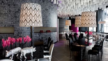 Un interno moderno caratterizzato da pareti decorate con motivi, lampade a sospensione e un'area pranzo con sedie nere e un tavolo in vetro.