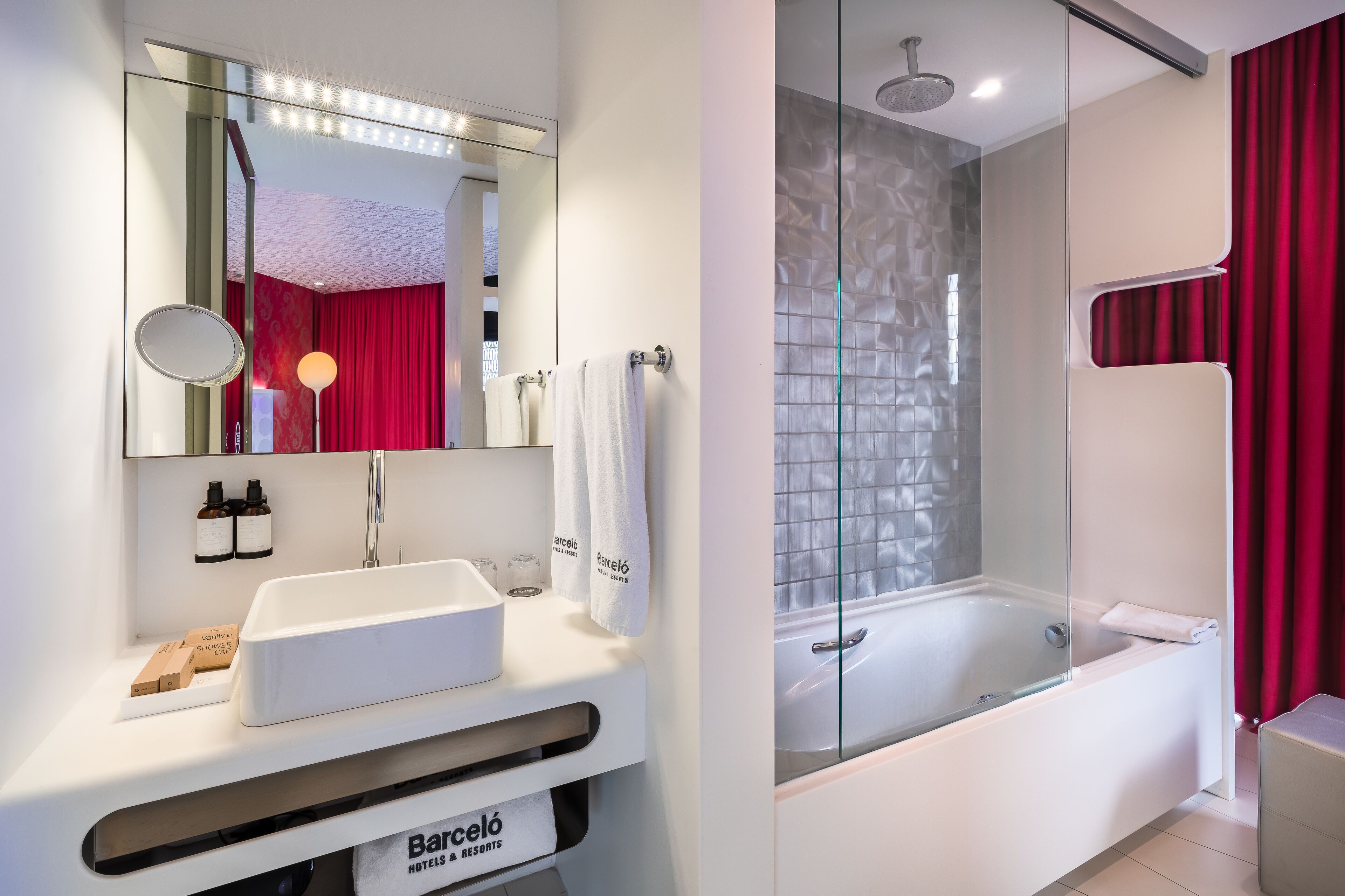 Un baño moderno con lavamanos blanco, espejo y ducha con mampara de vidrio.