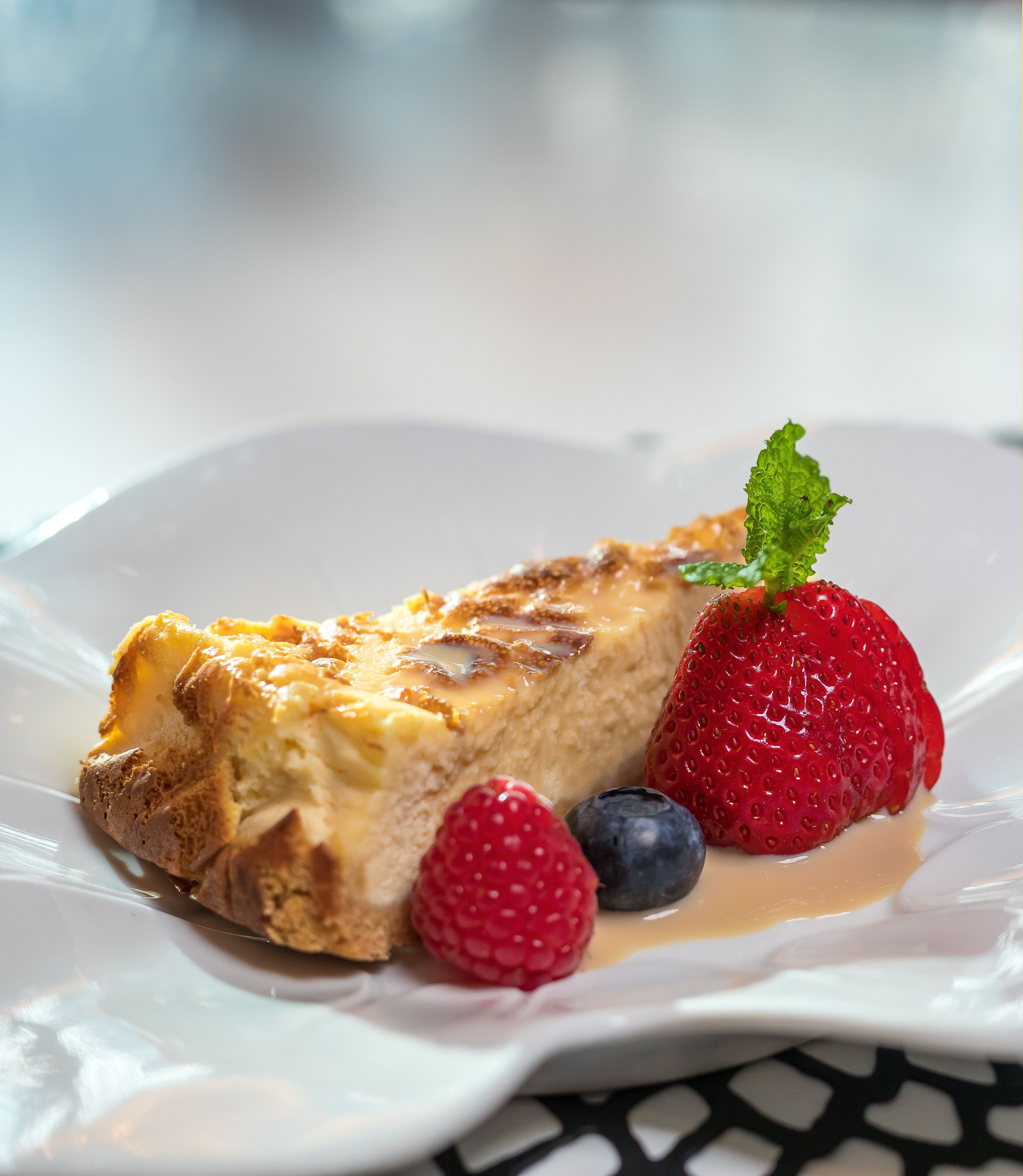Een stuk cheesecake met een aardbei en bosbessen op een wit bord.