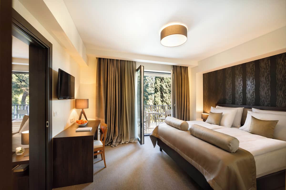 Una habitación de hotel con cama, escritorio, silla, lámpara y vistas al exterior.