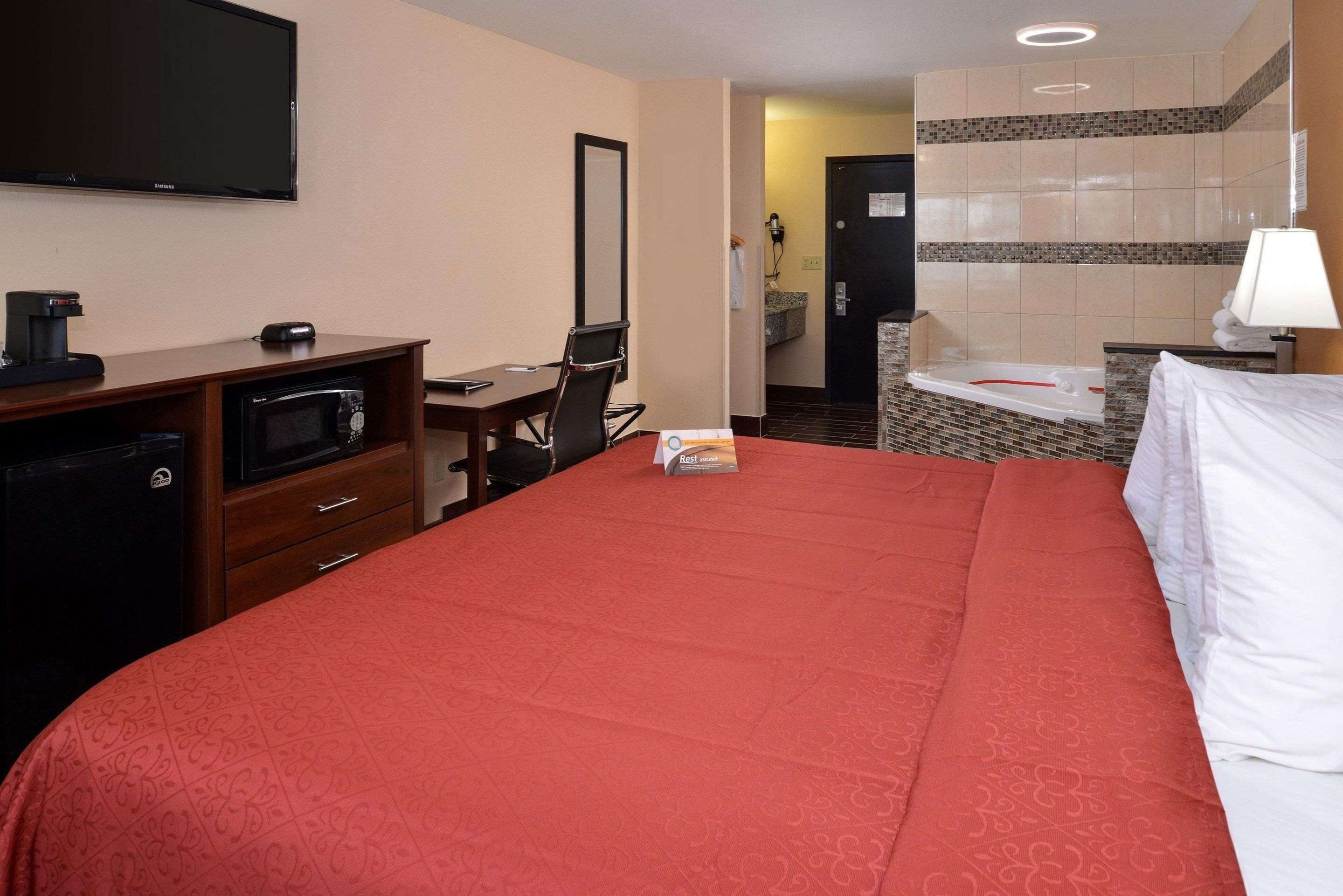 A hotel room with a bed, a desk with a computer, a microwave, a television, and a bathroom with a bathtub.