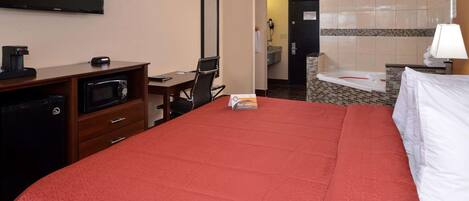 A hotel room with a bed, a desk with a computer, a microwave, a television, and a bathroom with a bathtub.