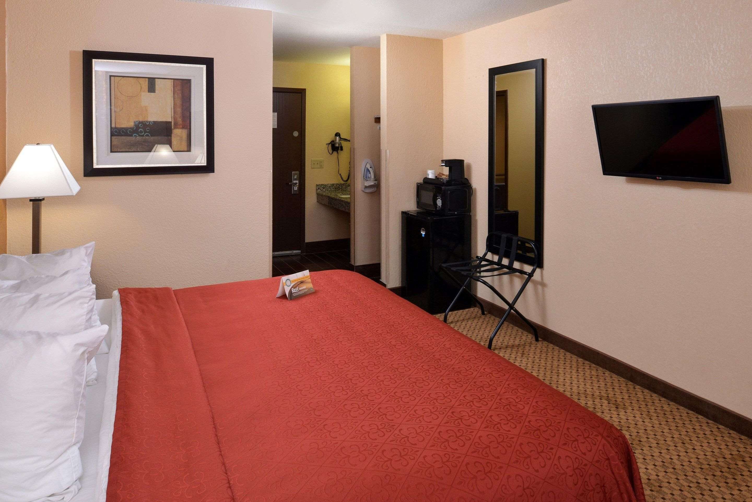 A hotel room with a bed, a desk with a chair, a television, and a framed picture on the wall.