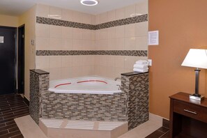 A bathroom with a large bathtub, tiled walls, a wooden bench, and a small table with a lamp.