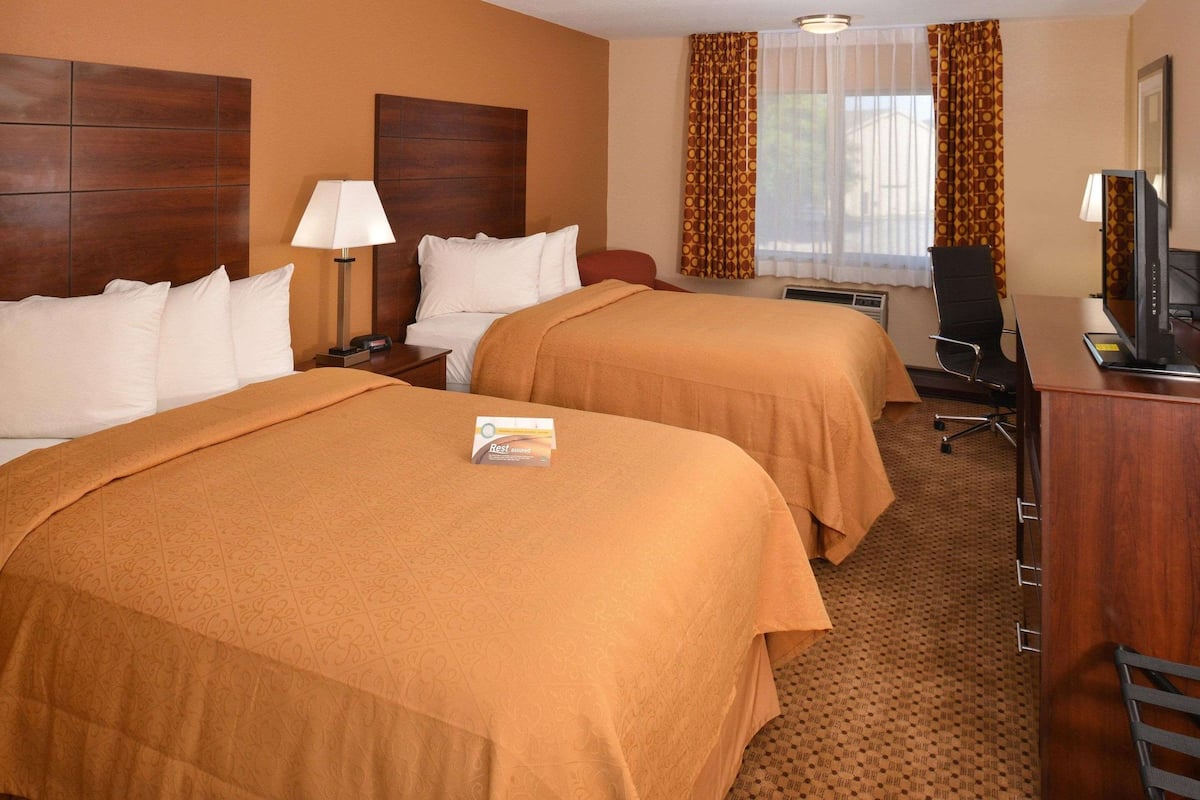 A hotel room with two beds, a desk with a computer, a chair, and a television.