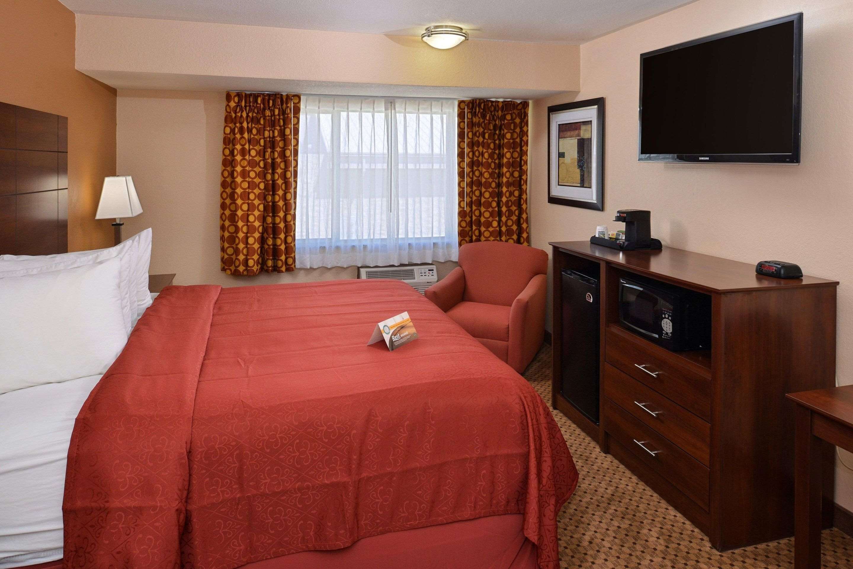 A hotel room with a bed, a desk with a television, a chair, a microwave, and a coffee maker.