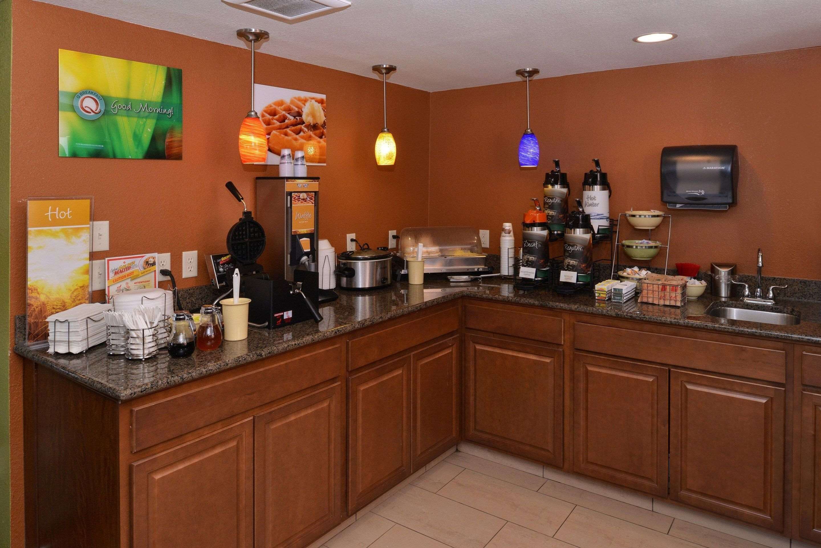 A kitchen with a granite countertop, wooden cabinets, a coffee station, and a microwave.