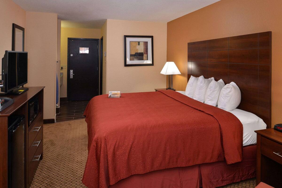 A hotel room with a large bed, a television on a dresser, a lamp, and a framed picture on the wall.