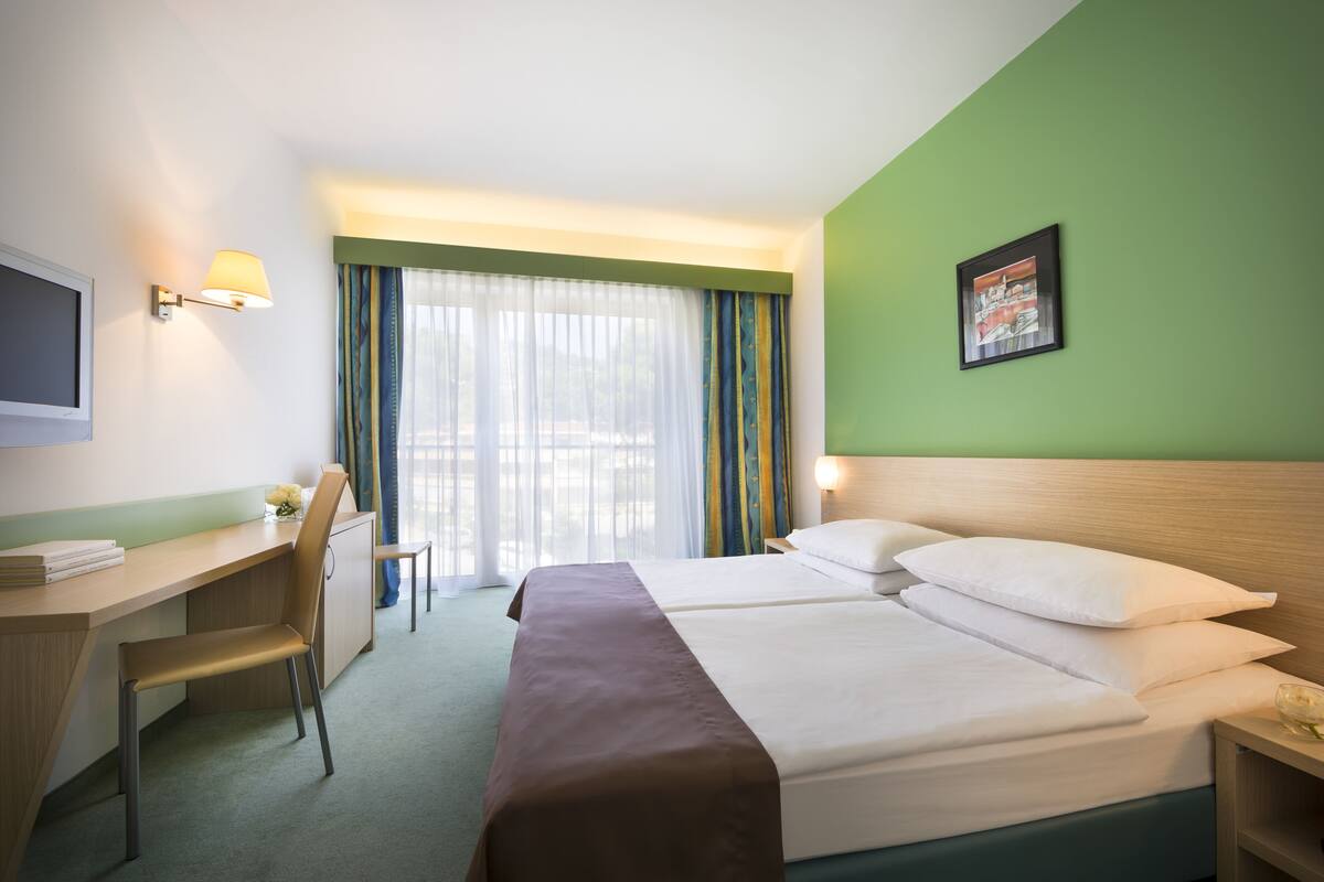 A hotel room with a bed, desk, chair, and a television.