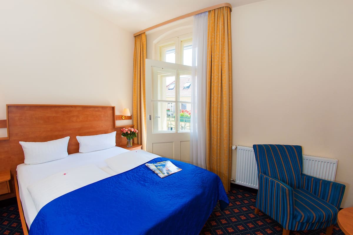 A hotel room with a bed, a chair, a window with curtains, and a radiator.