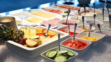 A buffet with various fruits and vegetables in bowls, including pineapple, orange, and cucumber slices.