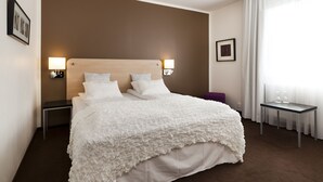 A hotel room with a large bed, two bedside tables, a small table with two wine glasses, and a purple stool. - Hotell Charlottenberg (Charlottenberg)