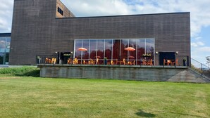 A modern building with a large glass facade, outdoor seating area with orange chairs, and a small staircase leading to the entrance. - Hotell Charlottenberg (Charlottenberg)