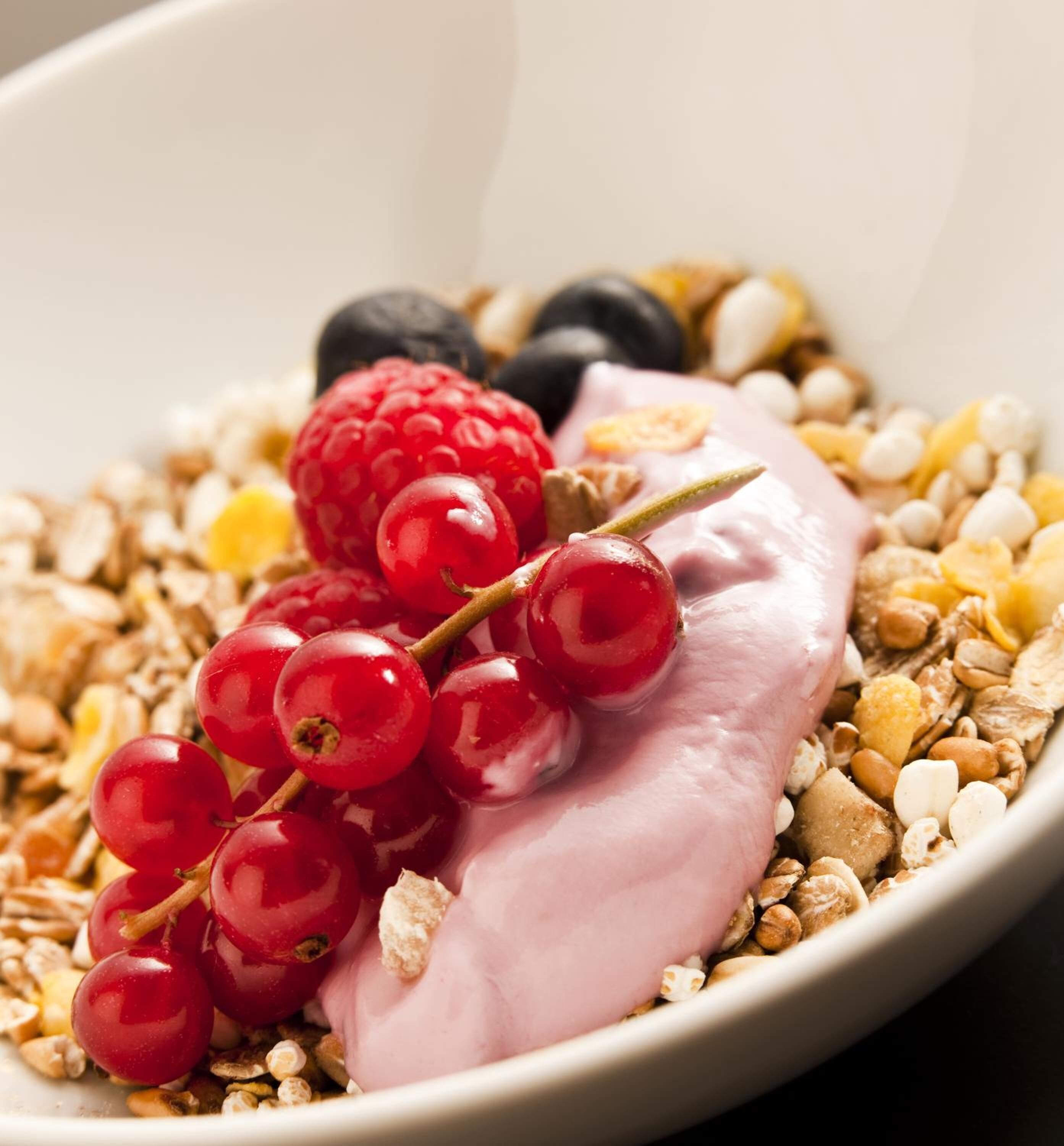 Un tazón de yogur con grosellas rojas y arándanos azules, rodeado de granola y nueces.