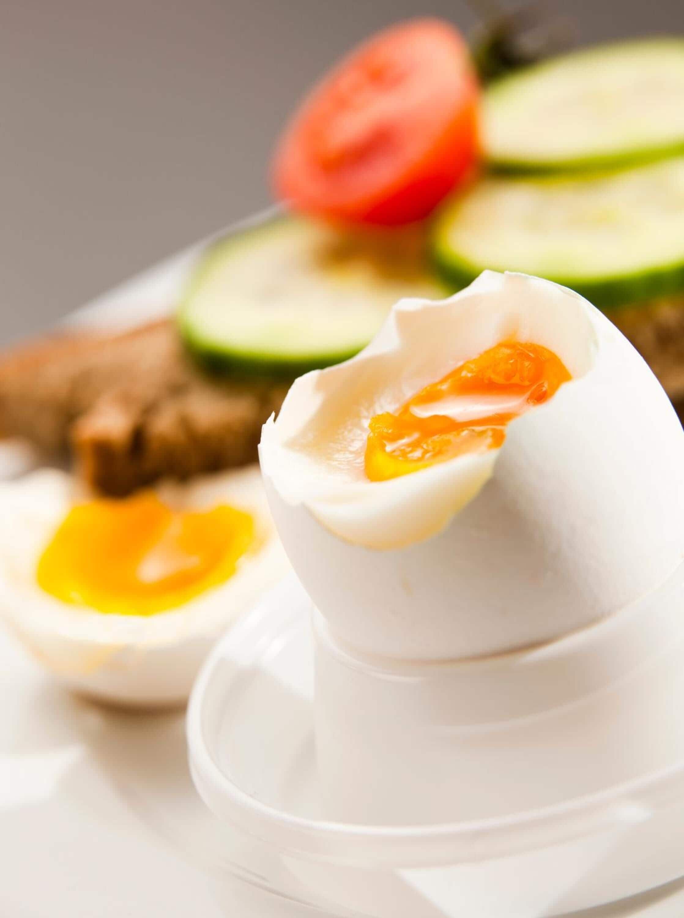 A boiled egg with a soft yolk, accompanied by sliced cucumbers and tomatoes on a white plate.