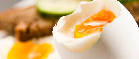 A boiled egg with a soft yolk, accompanied by sliced cucumbers and tomatoes on a white plate.