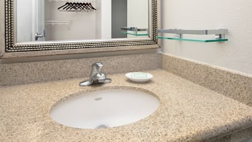 Un baño con encimera de granito, lavamanos blanco, espejo con marco decorativo y repisa de vidrio sobre el lavamanos.