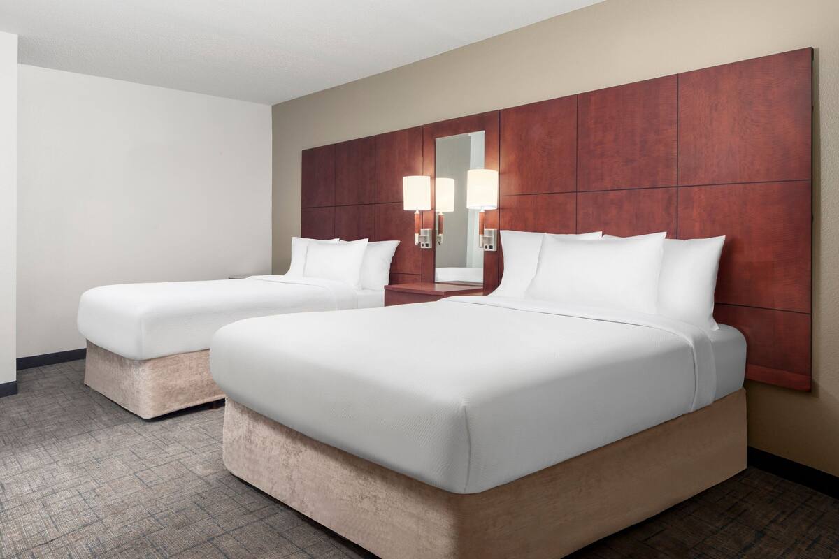Ein Hotelzimmer mit zwei Einzelbetten, einem Holzkopfstück, einem Spiegel und zwei Wandleuchten.