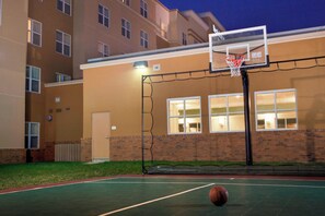Ein Basketballplatz im Freien neben einem Gebäude mit mehreren Fenstern und einer Tür.