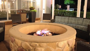 A stone fire pit with a fire burning, surrounded by wicker chairs and a patterned sofa. - Residence Inn Newport News Airport (Newport News)