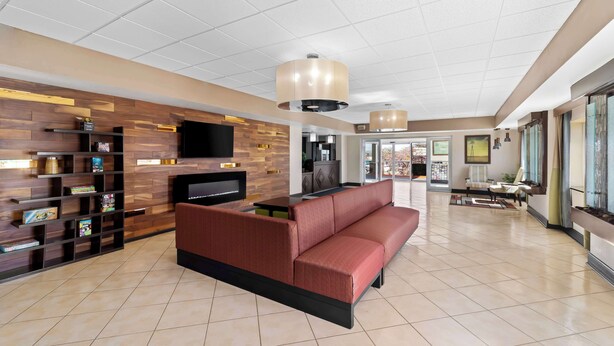 A modern lobby with a sectional sofa, a TV mounted on a wooden wall, and a bookshelf.
