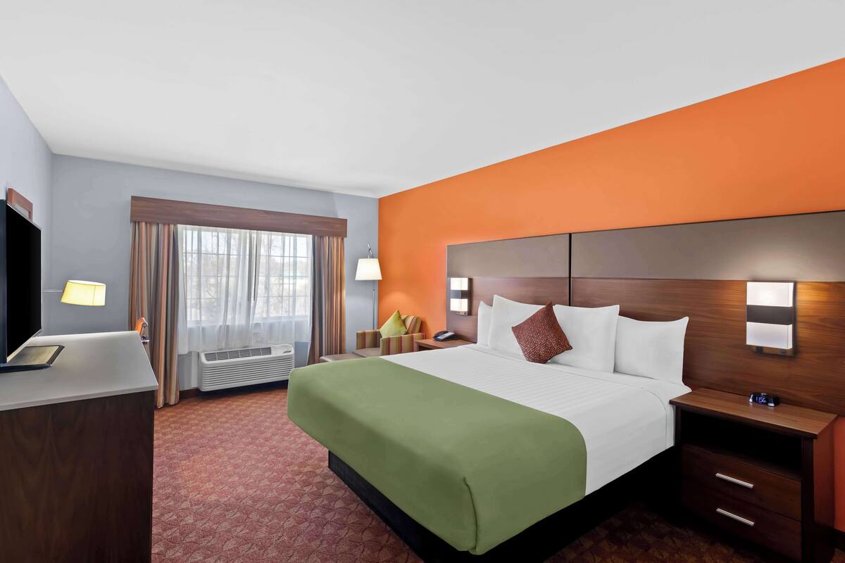 A hotel room with a large bed, a desk, a chair, a nightstand, and a window with curtains.